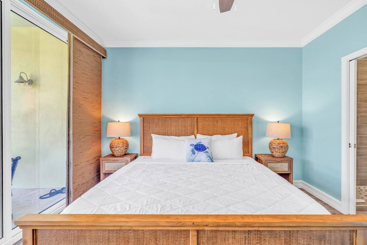 A bedroom with a large bed, two bedside tables with lamps, a wooden headboard, and a view of the outside through a sliding door.