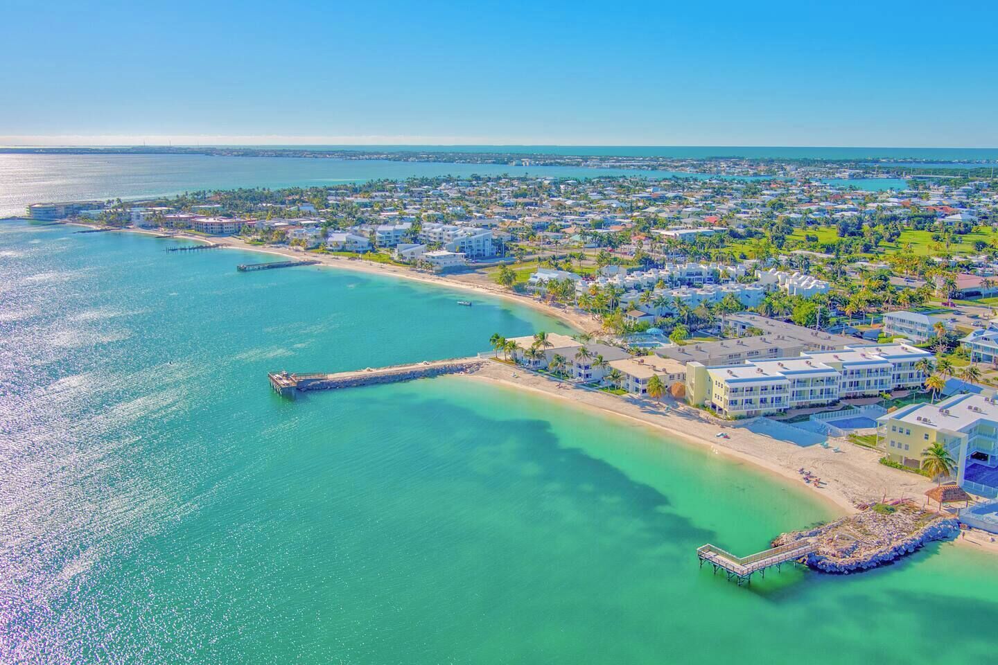 An aerial view of a coastal resort with beachfront properties, a pier, and a large hotel complex.