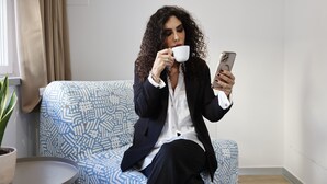 A person sitting on a patterned sofa in a room with a potted plant and a window with curtains. - New Pescara City b&b  (Pescara)