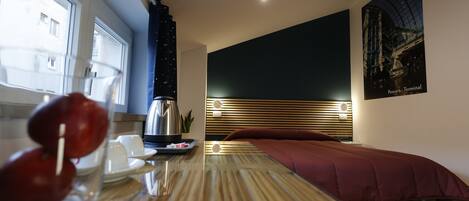 Una habitación moderna con una mesa de madera, una cama con colchón rojo, una mesita de noche, una tetera y un cartel en la pared.