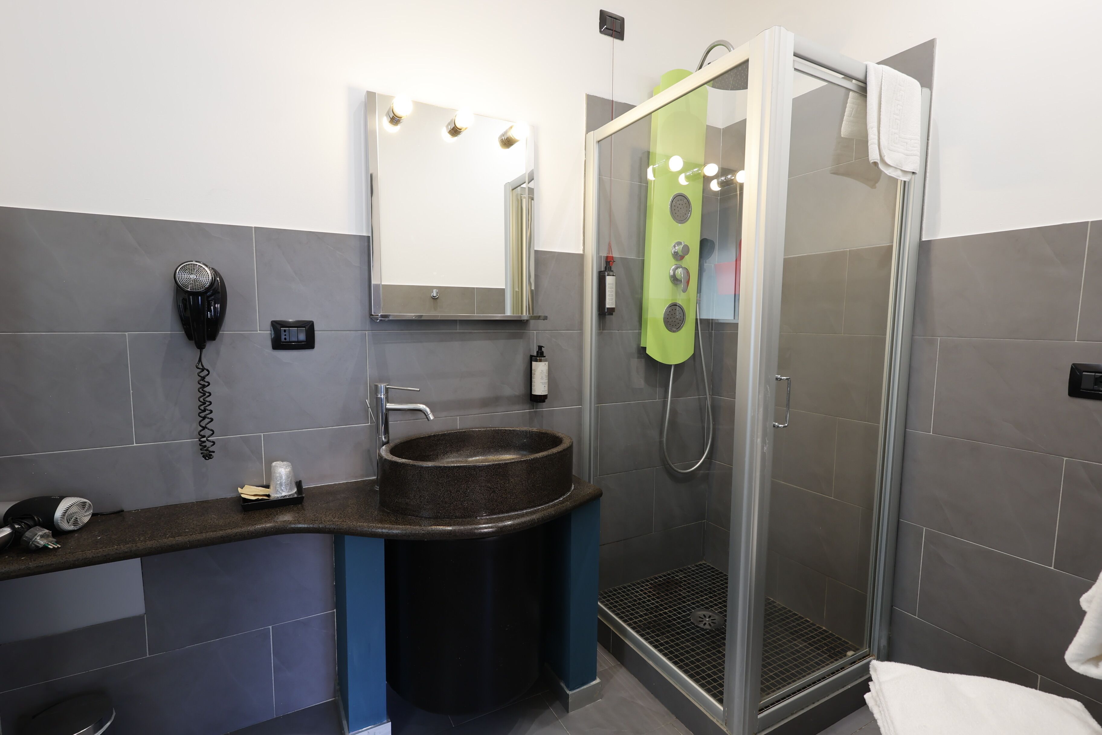 Une salle de bain moderne avec un grand miroir, un lavabo, un sèche-cheveux et une douche dotée d’une porte en verre.