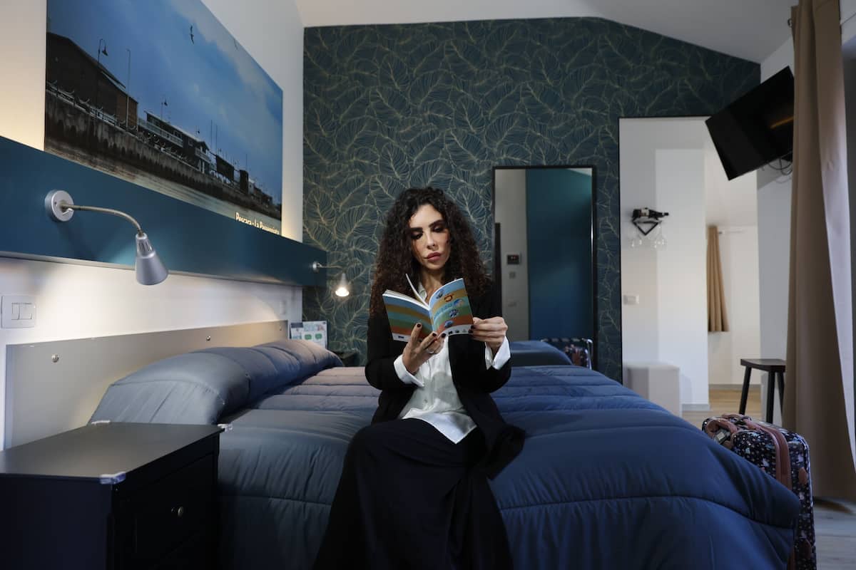 A person sitting on a bed in a hotel room, reading a book.