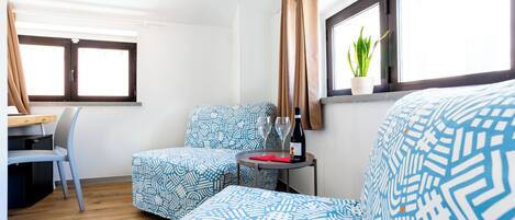 A room with a bed, a desk, a chair, a window with curtains, and a potted plant.