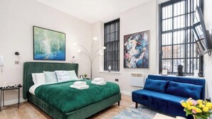 A bedroom with a green bed, a blue sofa, and artwork on the walls. - Stunning Apartment in Leeds (Leeds)