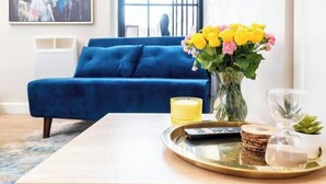 A living room with a blue sofa, a vase of yellow flowers, a tray with a remote control, a glass, and a candle. - Stunning Apartment in Leeds (Leeds)