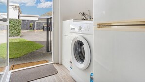 Une buanderie moderne équipée d’un lave-linge et d’un sèche-linge à chargement frontal, d’un petit évier et d’une porte donnant sur un espace extérieur abrité.