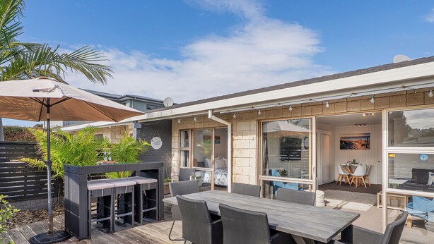 Une terrasse extérieure dotée d’une plateforme en bois, d’une table à manger avec des chaises, d’un barbecue et d’un espace salon couvert avec des parasols.