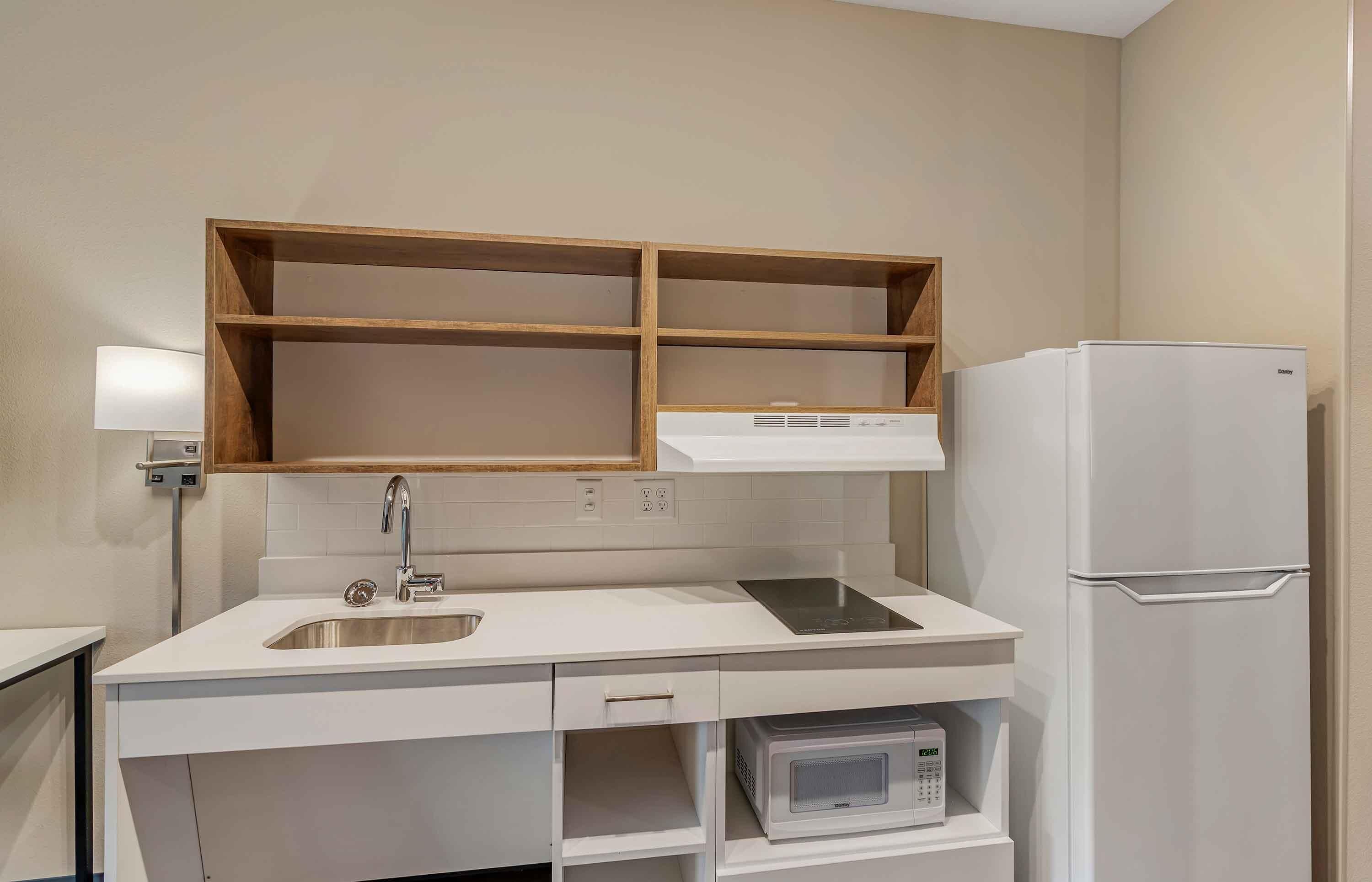 Una kitchenette compacta con microondas integrado, un lavamanos de acero inoxidable y un refrigerador blanco.