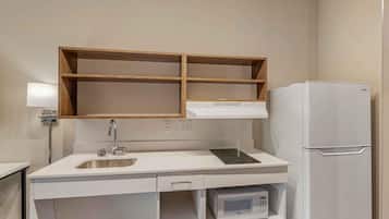 Una kitchenette compacta con microondas integrado, un lavamanos de acero inoxidable y un refrigerador blanco.