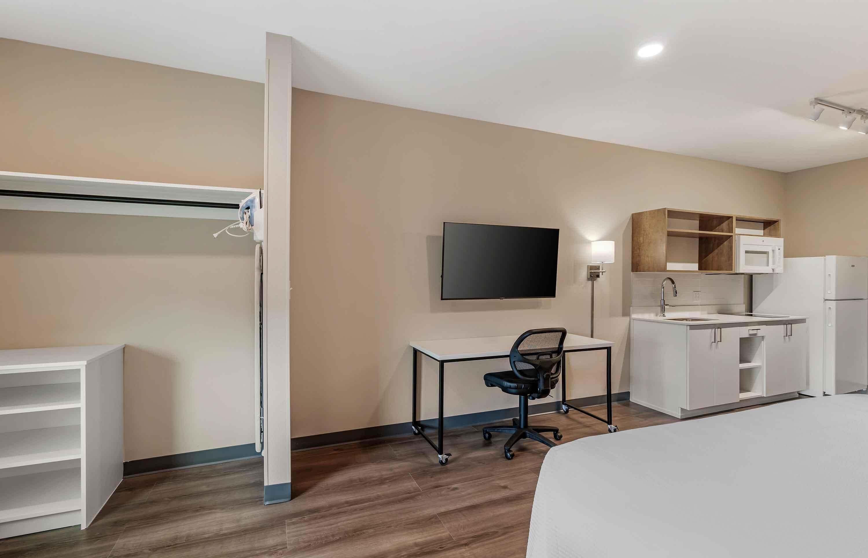 Habitación de hotel con cama, escritorio con silla, televisión de pantalla plana, microondas, refrigerador y armario empotrado.