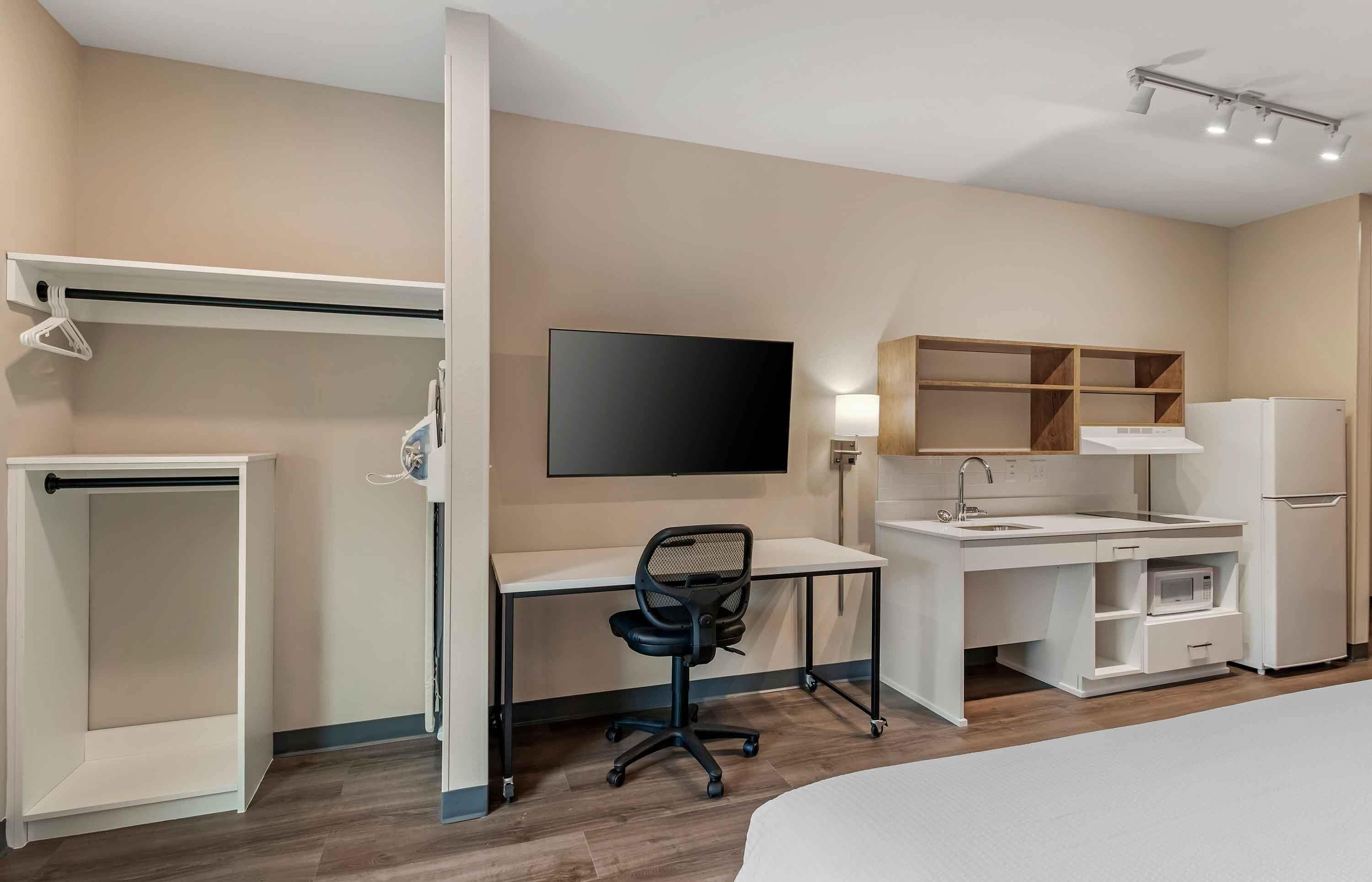 Une chambre d’hôtel comprenant un lit, un bureau avec une chaise, une télévision, une armoire, un four à micro-ondes et un réfrigérateur.