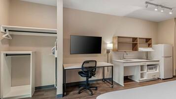 Habitación de hotel con cama, escritorio con silla, televisor, armario, microondas y refrigerador.