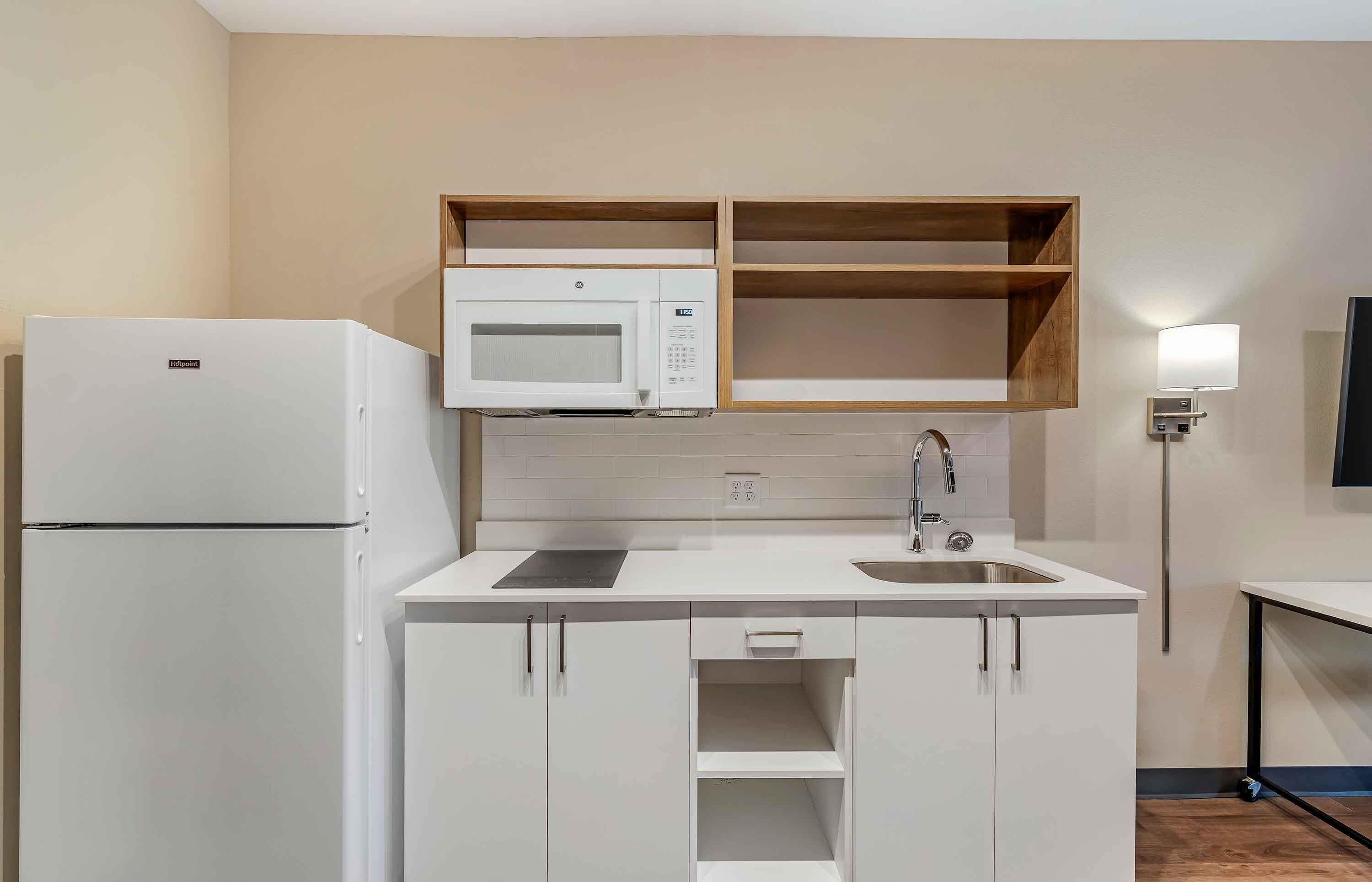 Una cocina compacta con muebles blancos, un microondas integrado, un lavamanos y un refrigerador.