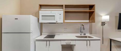 Una cocina compacta con muebles blancos, un microondas integrado, un lavamanos y un refrigerador.