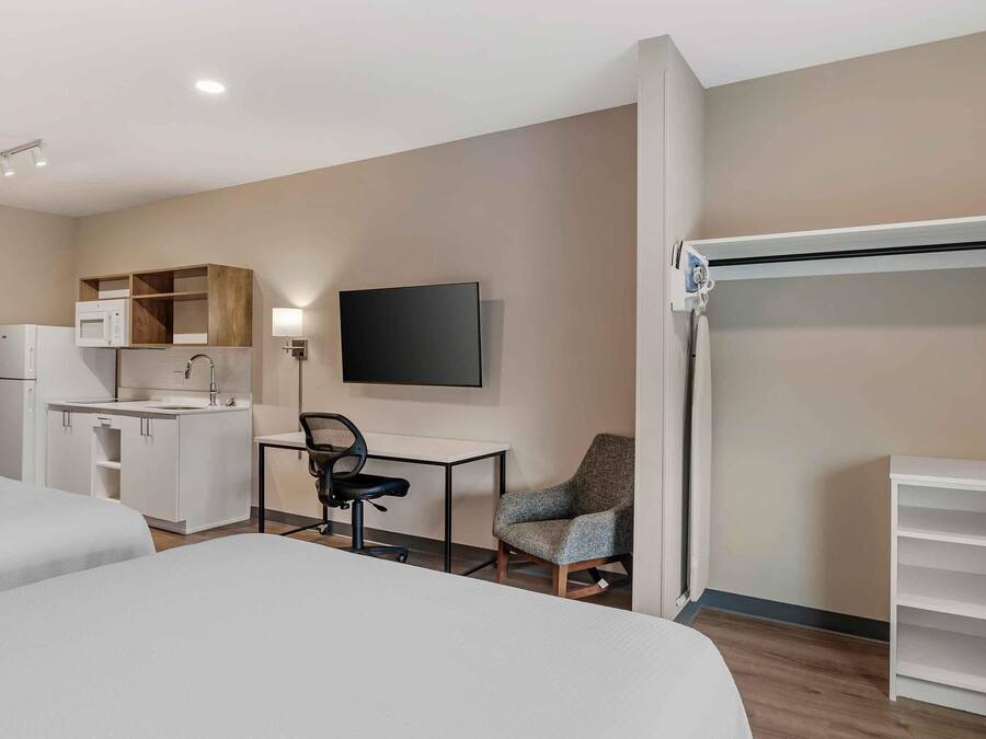 Une chambre d’hôtel avec deux lits, une kitchenette, un bureau avec une chaise, une télévision et une armoire.
