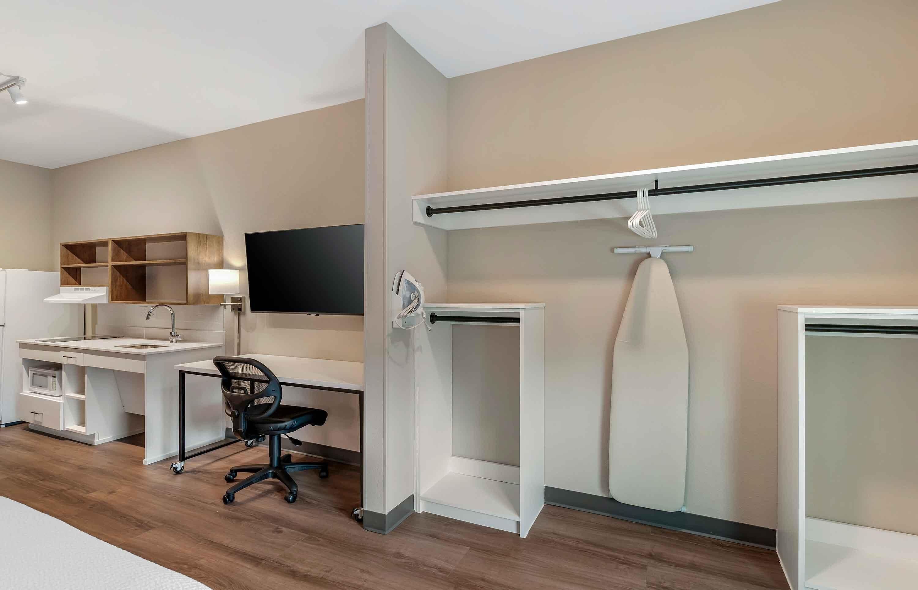 Un espace de bureau moderne avec un bureau blanc, un fauteuil de bureau noir et un téléviseur à écran plat fixé au mur.
