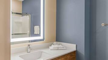A modern bathroom with a large mirror, a white sink, and a wooden vanity.