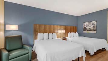 Habitación de hotel con dos camas, cabecero de madera, sillón verde y un cuadro con paisaje de montaña en la pared.