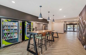 A modern indoor space with vending machines, a wooden table, and chairs. - Extended Stay America Premier Suites - Jacksonville - Airport (Jacksonville)