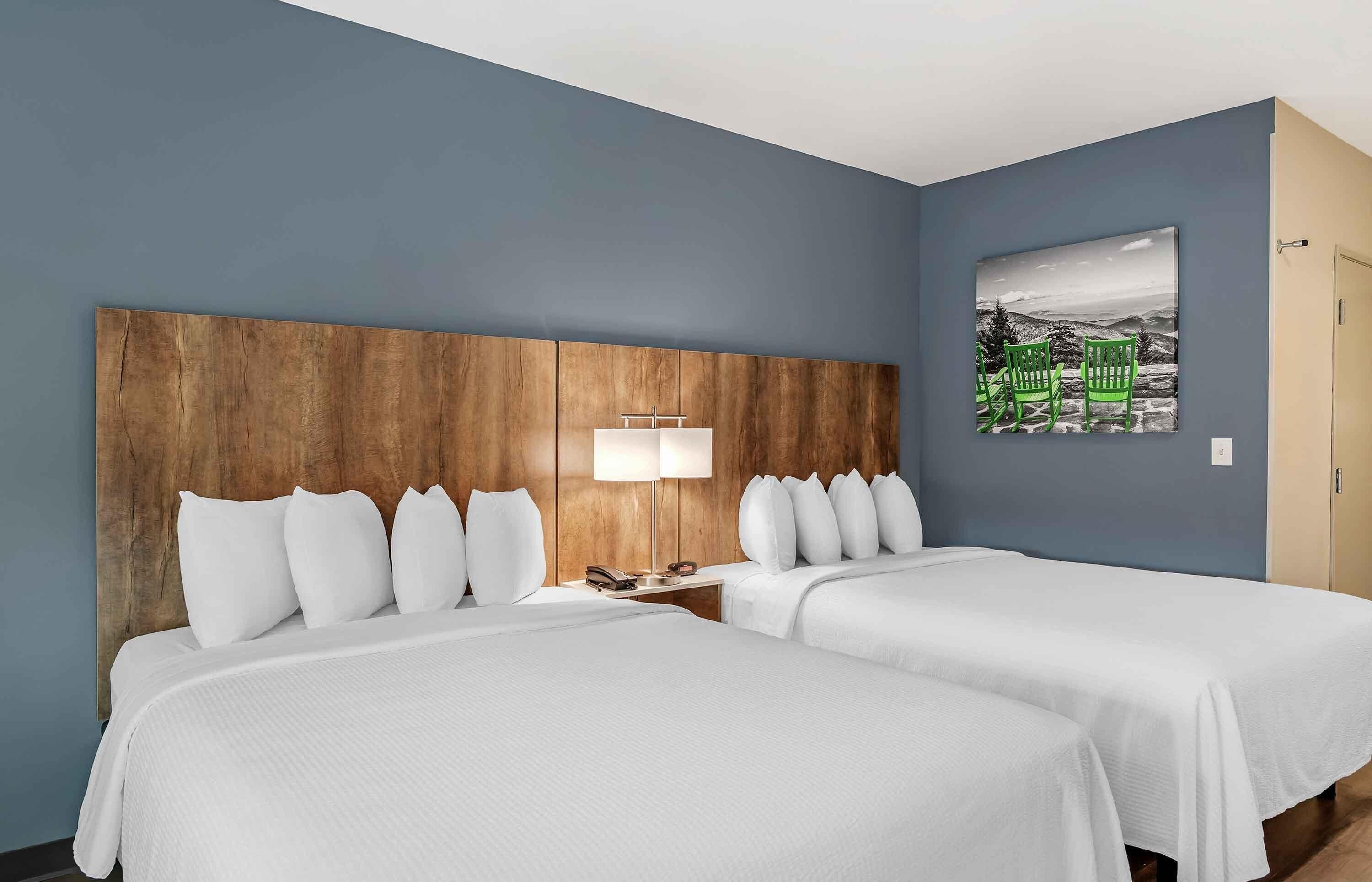 A hotel room with two beds, a wooden headboard, a nightstand with a lamp, and a painting on the wall.