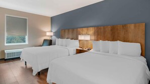 A hotel room with two beds, a wooden headboard, bedside lamps, a chair, and a window with a view.