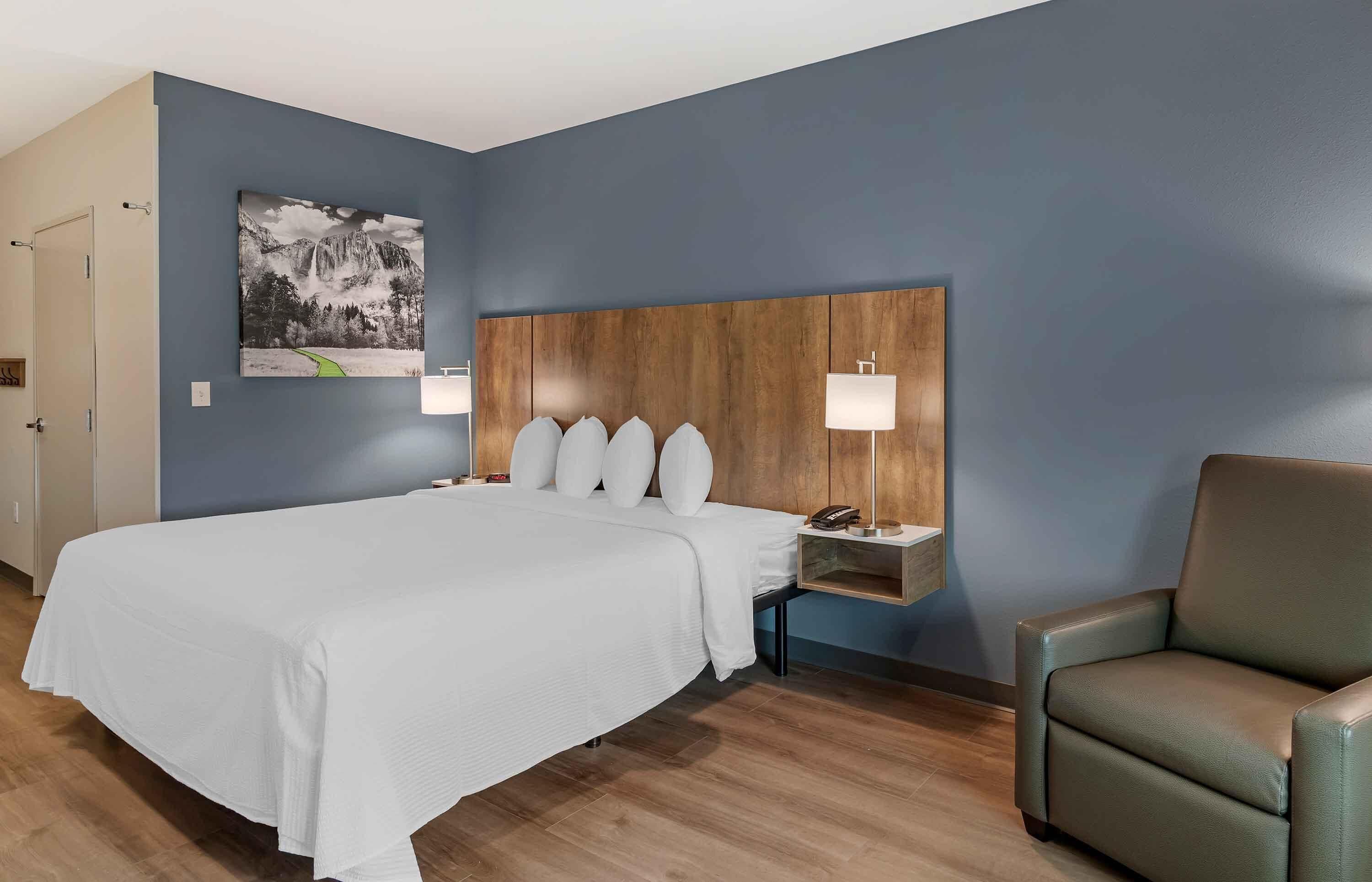 Ein Hotelzimmer mit einem großen Bett, einem Holzkopfende, einem Nachttisch mit Lampe und einem Sessel.