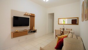 A modern living room with a flat-screen TV, wooden entertainment unit, dining table, and a large mirror. - SUH Copacabana 63 Peace Beach (Rio de Janeiro)
