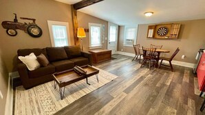 A living room with a brown sofa, a coffee table, and a dining area with a table and chairs. - Hoppy Hill Farm House (Dover Plains)