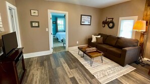 A living room with a brown couch, a coffee table, a TV stand, and a patterned rug. - Hoppy Hill Farm House (Dover Plains)