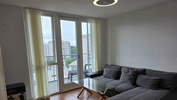 A modern living room with a grey sofa, a glass coffee table, and a view of the city through large windows. - Exceptional Two-Bedroom Apartment in the City Center. (Birmingham)