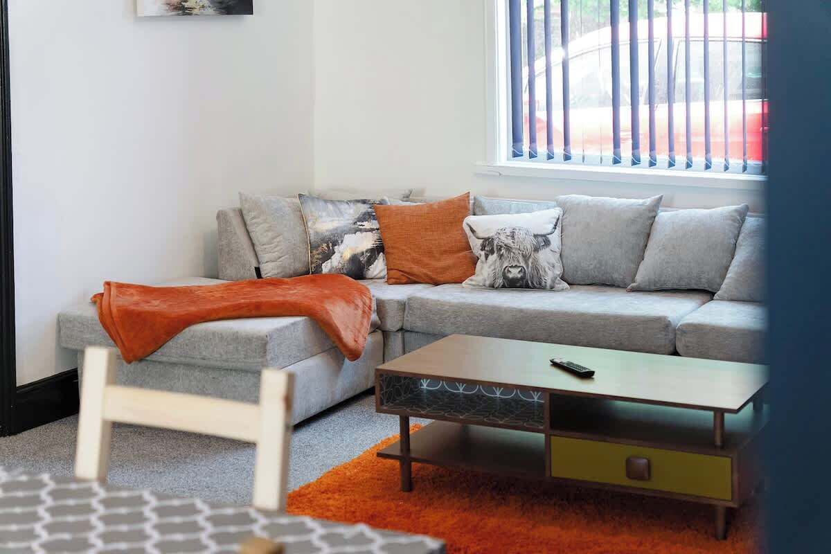 En moderne stue med en grå sofa, et orange pled og et sofabord.