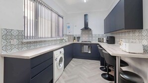 A compact kitchen with a washing machine, a built-in oven, and a coffee maker.
