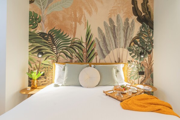 A bedroom with a bed, pillows, a bedside table with a plant, and a tray with food and drink.