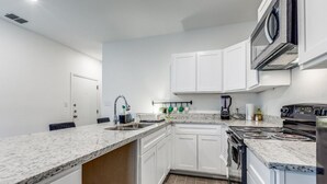 A modern kitchen with white cabinets, granite countertops, a built-in oven, and a microwave.