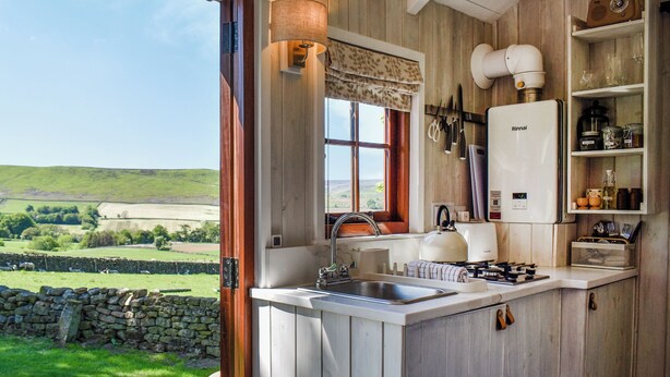 A rustic kitchen with a view of rolling hills, a stone wall, and a wooden door. - Barn Owl Hut - UK49769 (Westerdale, near Whitby)