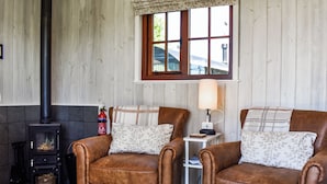A cozy room with two brown leather armchairs, a small table with a lamp, a window with a view, and a wood-burning stove. - Barn Owl Hut - UK49769 (Westerdale, near Whitby)
