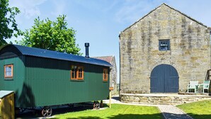 A green train car and a stone building with a large door and windows. - Barn Owl Hut - UK49769 (Westerdale, near Whitby)