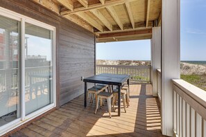 A wooden deck with a table and chairs, overlooking a beach. - Deck & View: Oceanfront Oasis in Oak Island! (Oak Island)