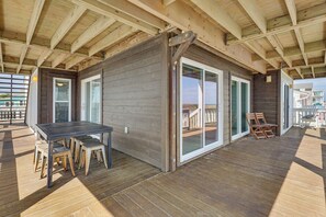 A covered outdoor deck with a wooden table and chairs, large sliding glass doors, and a view of the ocean. - Deck & View: Oceanfront Oasis in Oak Island! (Oak Island)