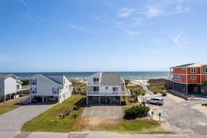 A coastal property with a two-story house featuring a balcony, a driveway, and a view of the ocean. - Deck & View: Oceanfront Oasis in Oak Island! (Oak Island)