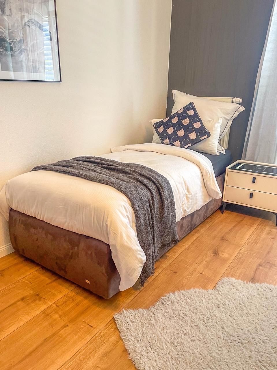 Une chambre à coucher avec un lit, des tables de chevet, une commode, un tapis gris et un tableau au mur.