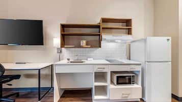 A compact kitchen with a microwave, refrigerator, and wooden shelves.