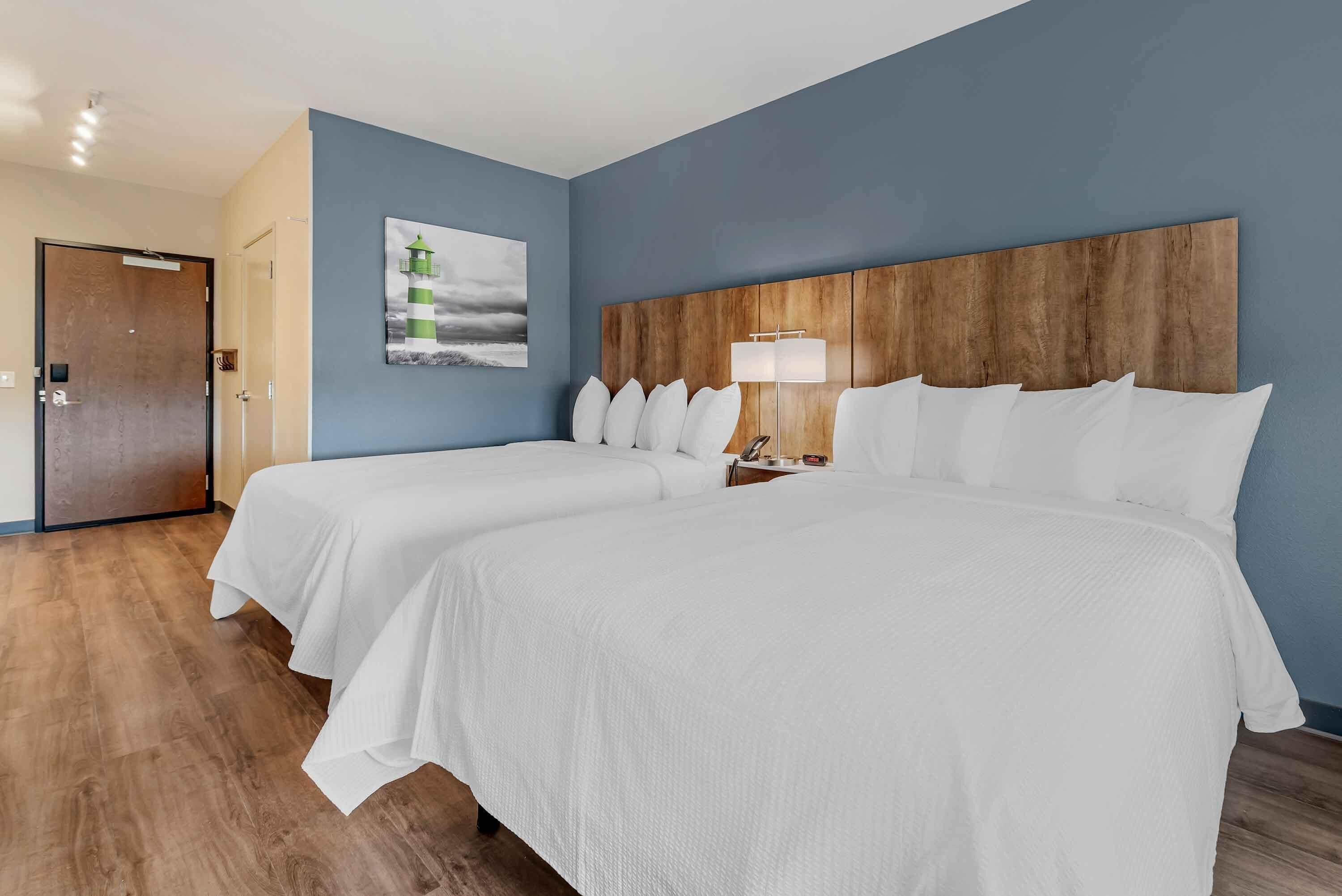 Een hotelkamer met twee bedden, een houten hoofdeinde, een nachtkastje met een lamp en een schilderij aan de muur.