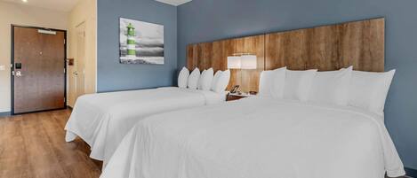 Ein Hotelzimmer mit zwei Betten, einem Holzkopfende, einem Nachttisch mit Lampe und einem Gemälde an der Wand.