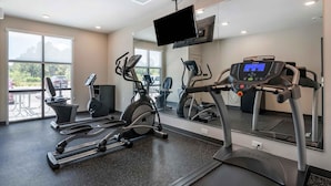 Un gimnasio con cintas de correr, elípticas y un espejo grande.