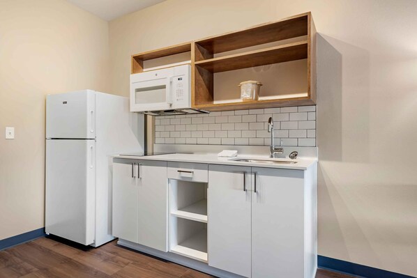 Una cocina compacta con muebles blancos, un microondas integrado y un lavamanos.