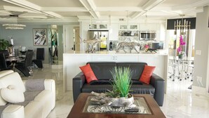 Un salon moderne avec un canapé en cuir noir, un fauteuil blanc et une table basse en bois agrémentée d’objets décoratifs.
