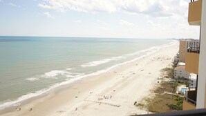 Une vue sur la plage, avec un ciel dégagé, un rivage sablonneux et des bâtiments le long de la côte.
