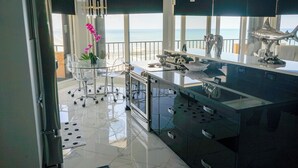 Une cuisine moderne dotée d’un grand îlot central, d’appareils électroménagers en acier chromé et offrant une vue sur l’océan.
