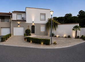 A modern two-story house with a garage, a well-maintained garden, and a street lamp.